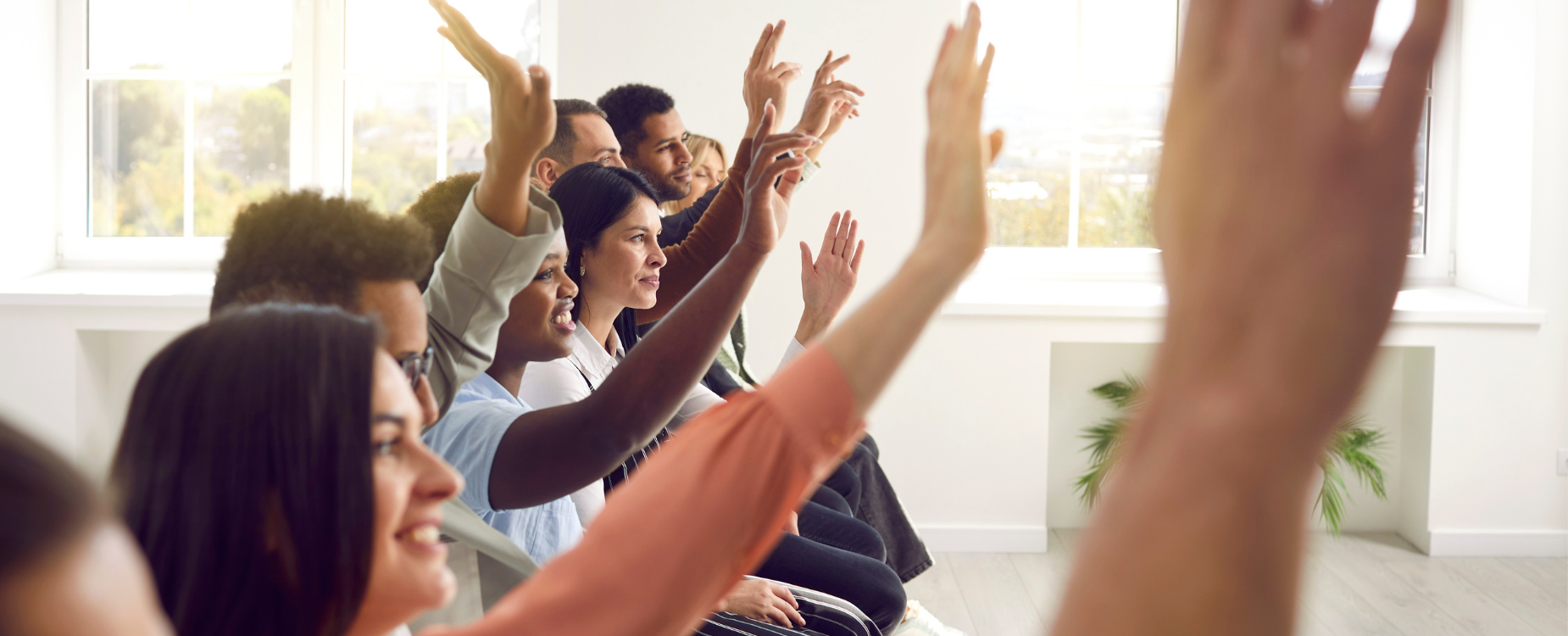 People seated in a group raise their hands during an indoor session, showing participation, community involvement, and shared action.