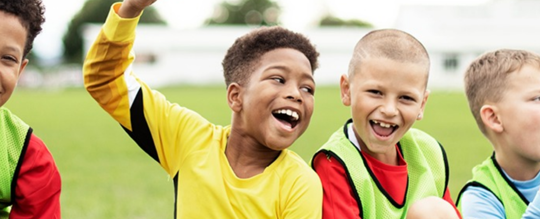 Smiling children in colourful sports bibs play together outdoors, promoting inclusion and teamwork in sport.