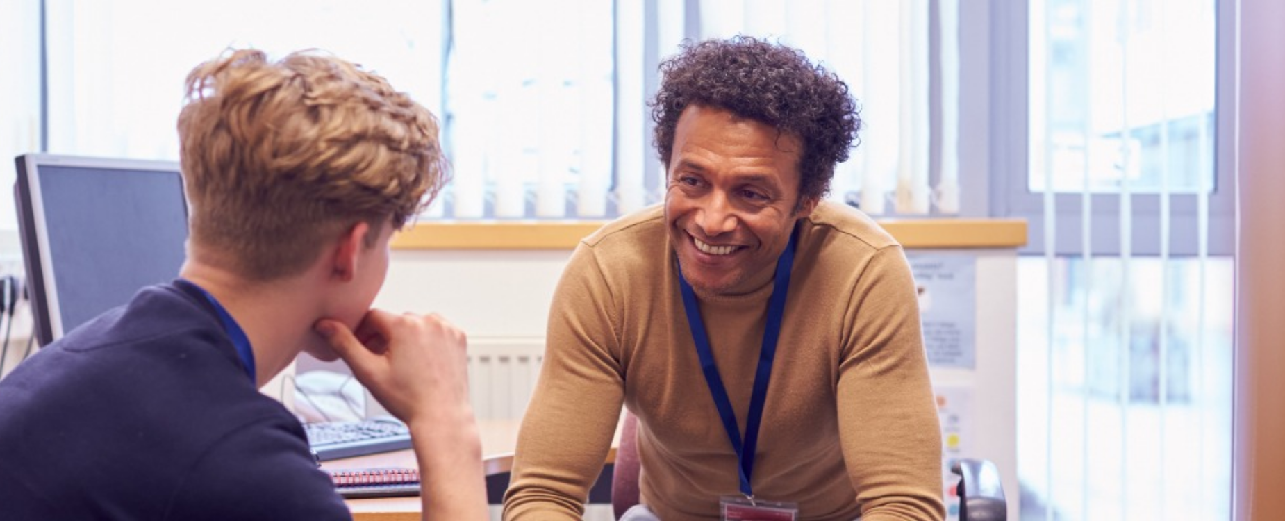 A support worker smiles while speaking with a young person during a one-to-one meeting in an office.