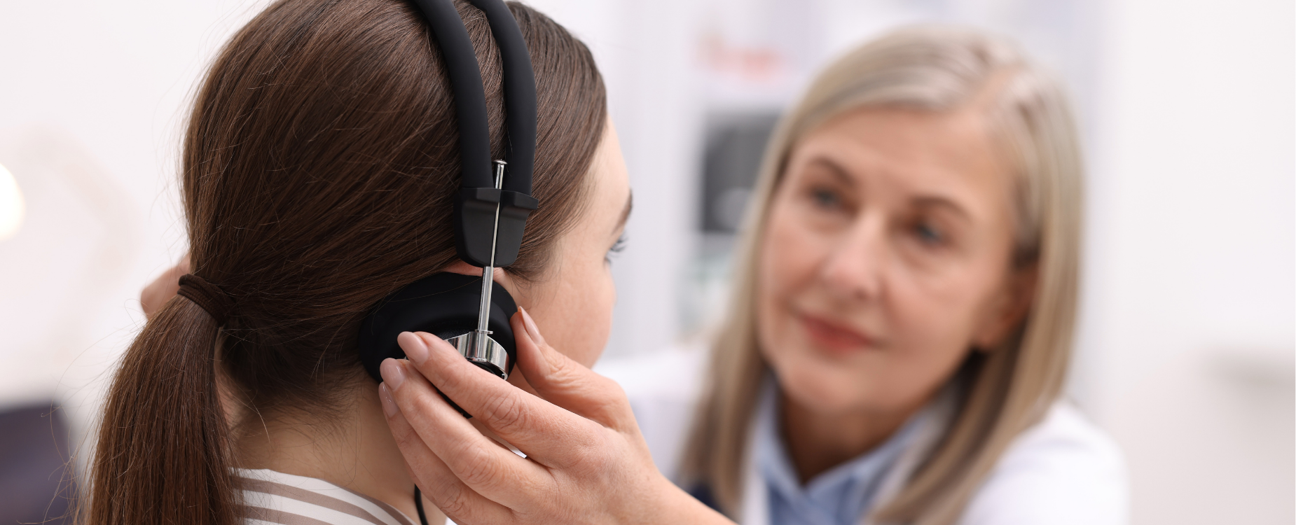 Clinician adjusts headphones on a patient during a hearing test, representing professional hearing assessment and support.