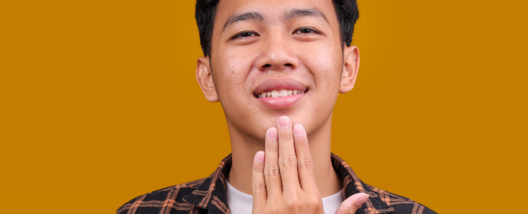 A man signing an NZSL sign against a yellow background, representing sign language learning and communication.