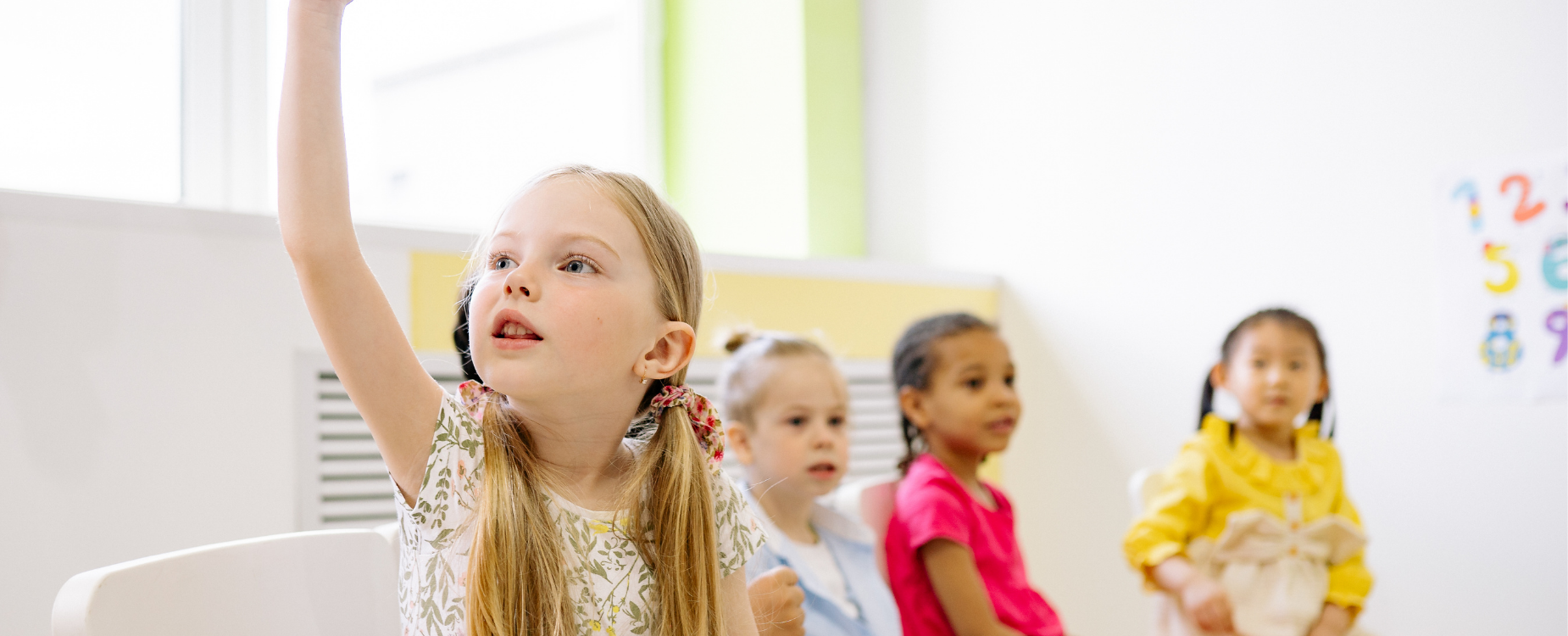 Young girl raises her hand in a classroom, representing children&rsquo;s learning and the lasting impact of support for Deaf children and families.