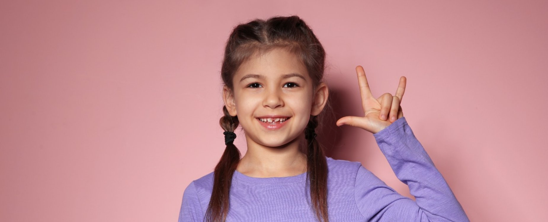 Smiling girl signing against a pink background, representing communication, partnership, and support.