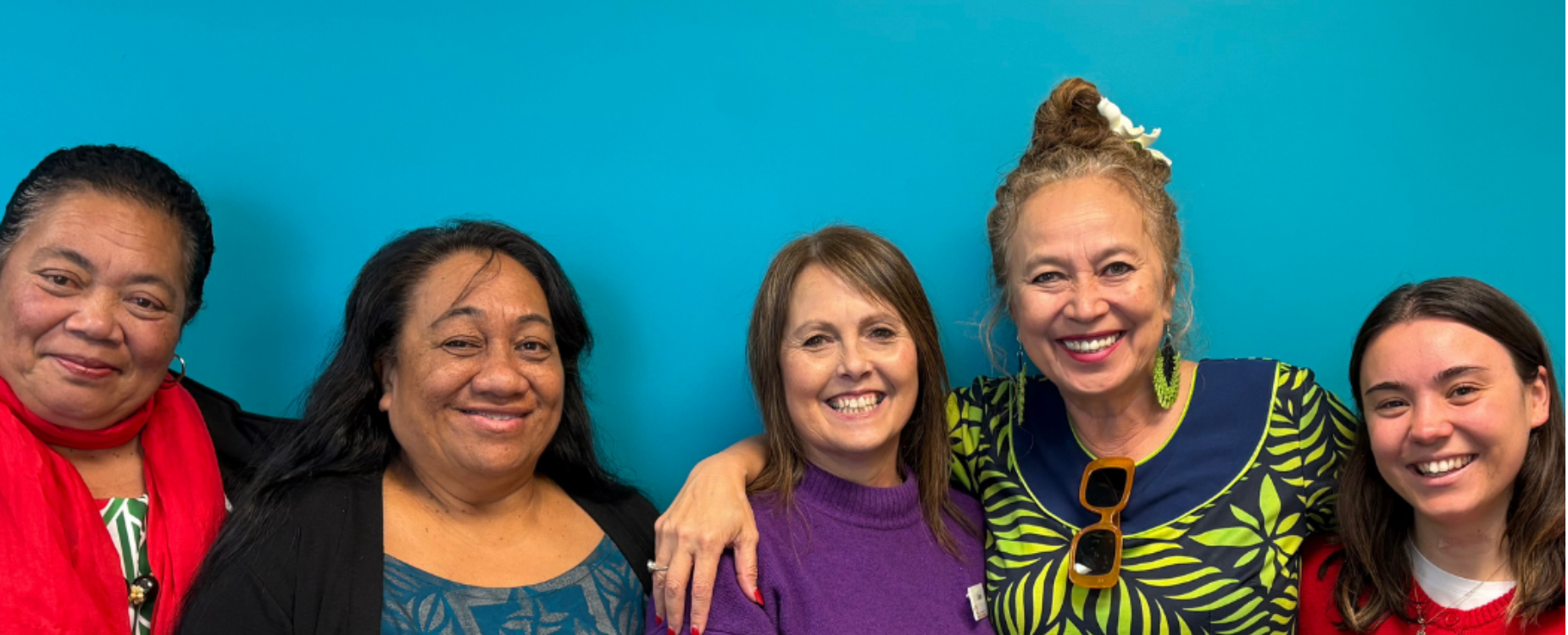 Five women standing together and smiling against a blue background.