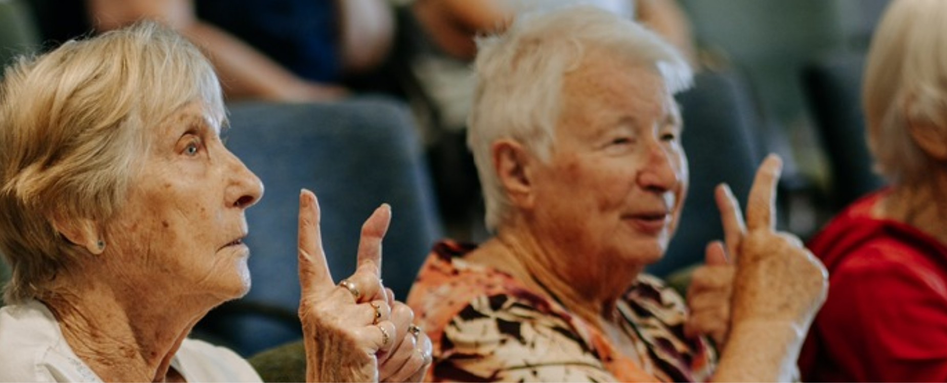 Older adults using sign language during a retirement village outreach session.