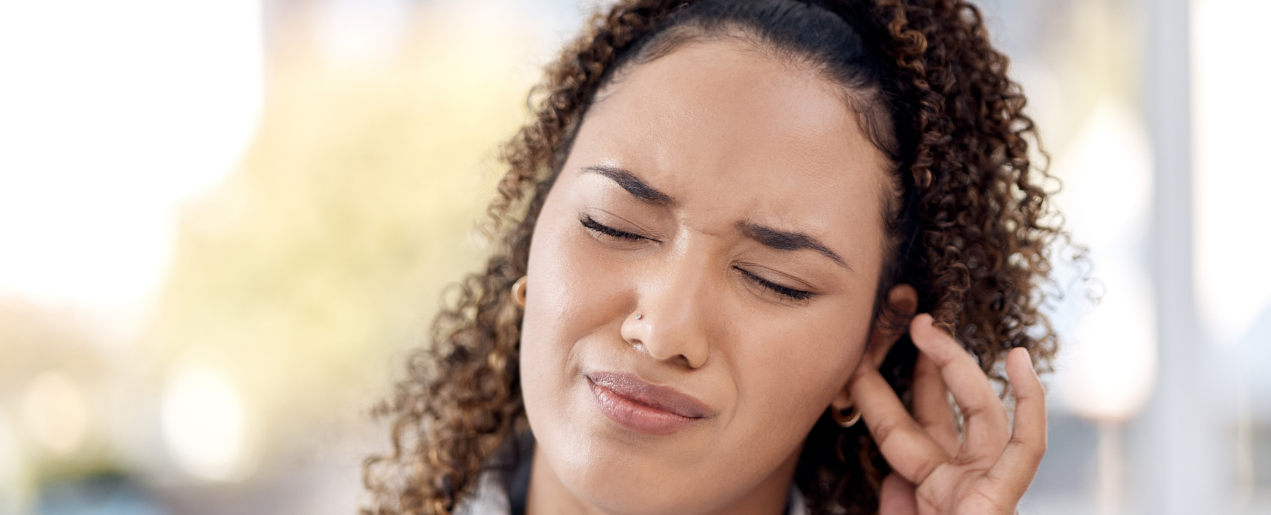 Woman touching her ear with a pained expression, representing tinnitus or ear-related discomfort.
