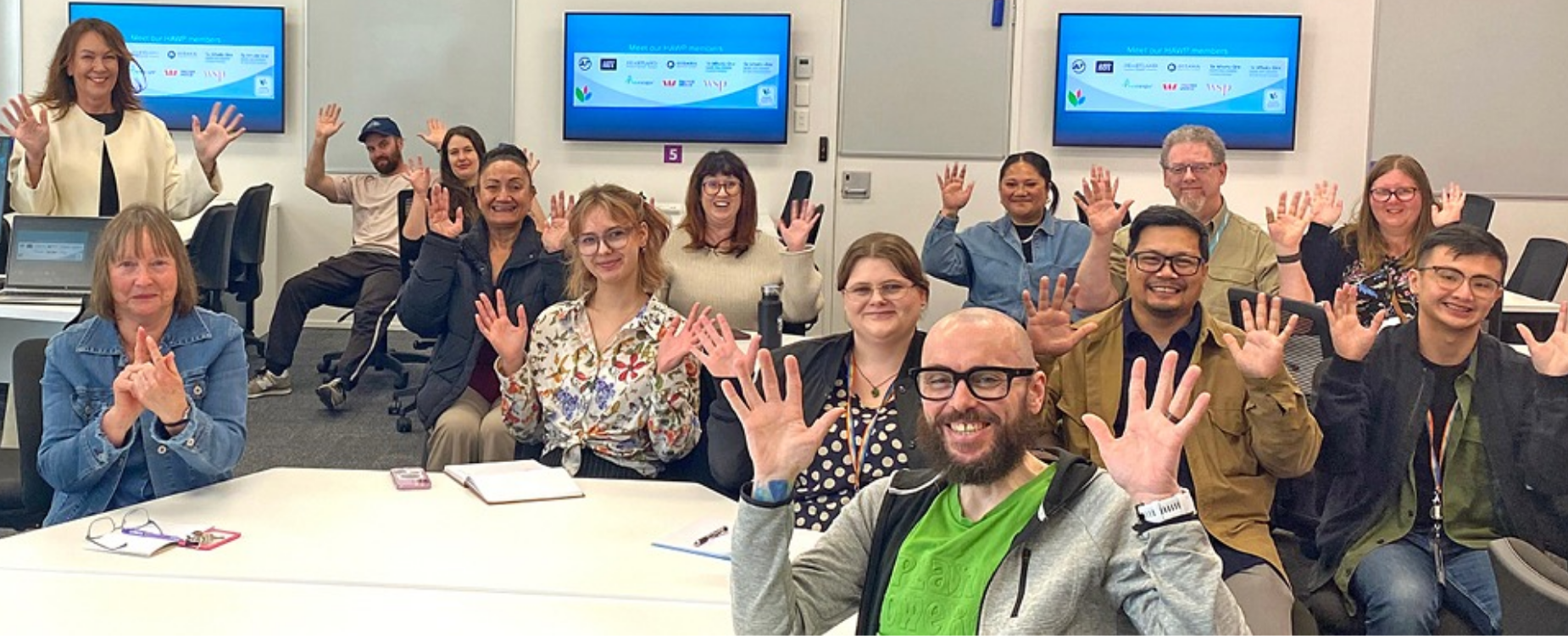 Group of adults smiling and waving during a Hearing Accredited Workplace training session.
